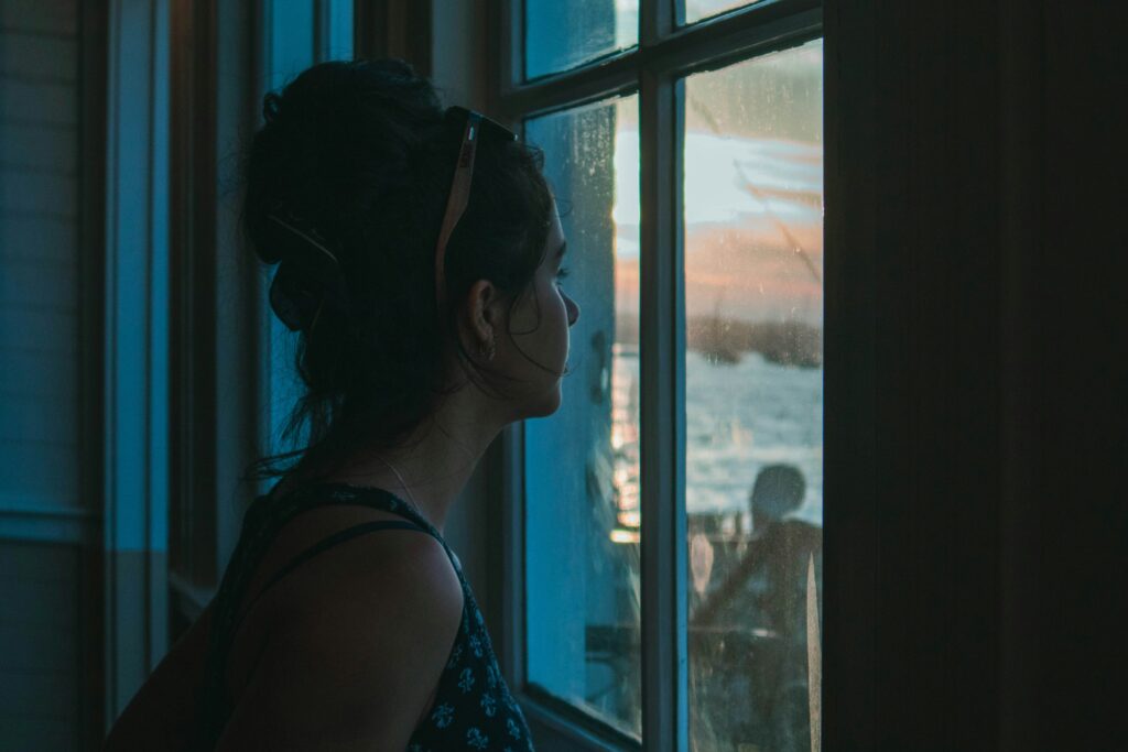 Person looking out a window, calm and grounded, representing the window of tolerance concept.