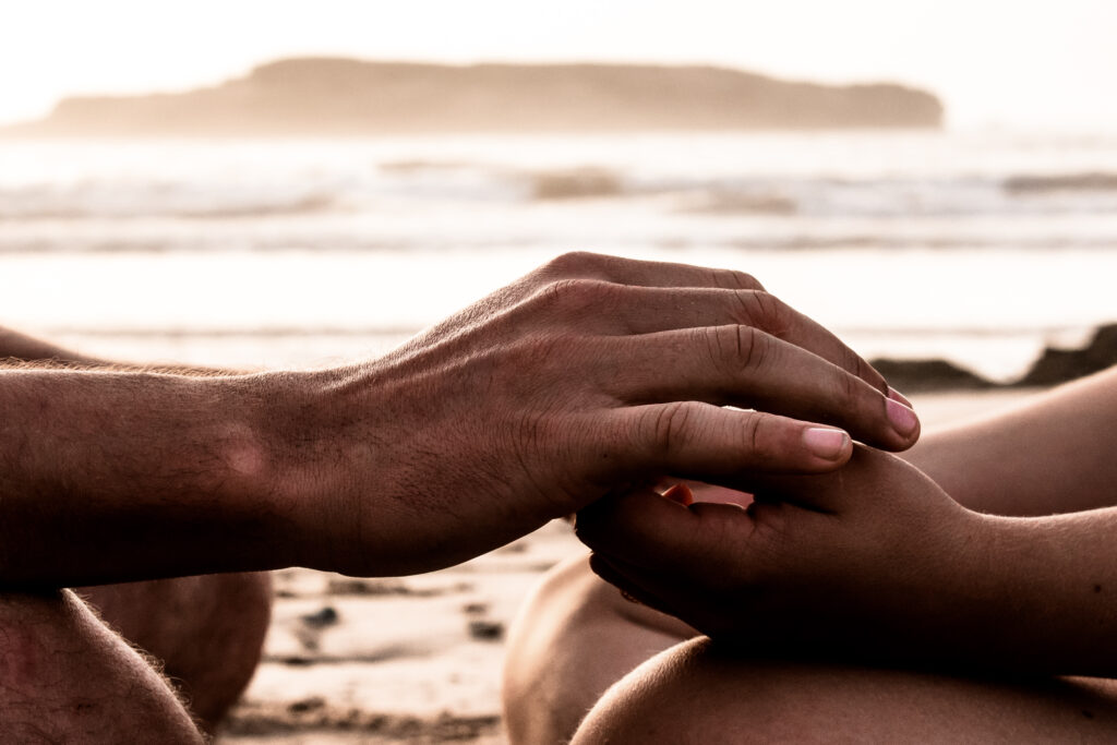 Two people sitting cross legged, facing each other, touching hands.